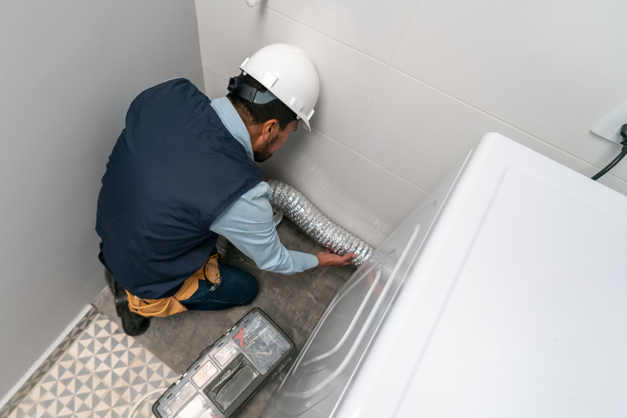 Technician installing dryer vent hose behind washer